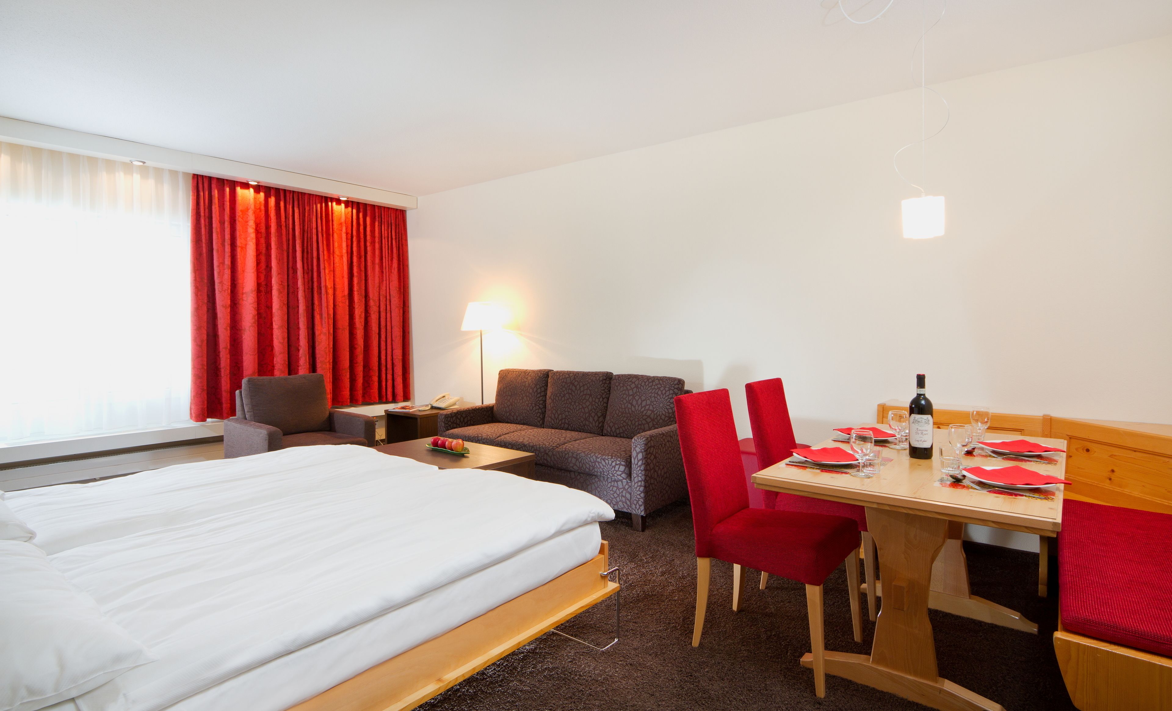 Una habitación de hotel con cama, sofá, mesa de comedor y silla, y una lámpara.