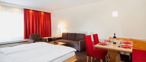 Una habitación de hotel con cama, sofá, mesa de comedor y silla, y una lámpara.