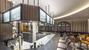 A modern bar area with a long counter, seating, and a kitchen in the background. - Central Apartments Davos (Davos)