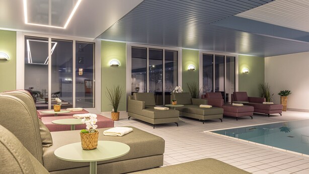 A modern indoor pool area with sofas, tables, and potted plants. - Central Apartments Davos (Davos)