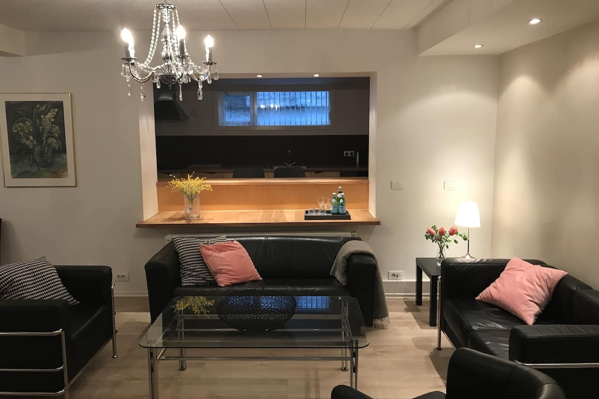 A modern living room with a black leather sofa, a glass coffee table, and a chandelier.