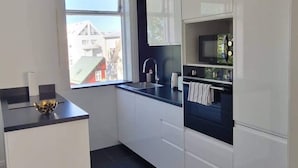 A modern kitchen with white cabinets, a black countertop, and a window providing a view of buildings outside. - Theater Row Apartments (Reykjavik)