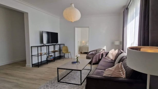A modern living room with a sofa, coffee table, TV, and a lamp. - Theater Row Apartments (Reykjavik)