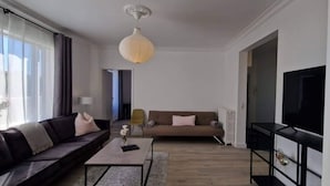 A modern living room with a sofa, a coffee table, a TV, and a lamp. - Theater Row Apartments (Reykjavik)