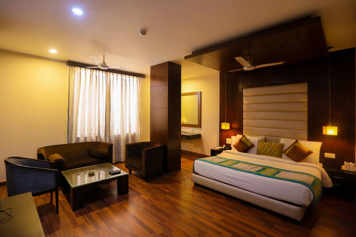 Una habitación de hotel con cama, sofá, mesa de centro, silla, escritorio y espejo.