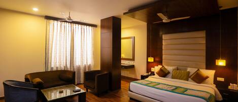 A hotel room with a bed, a sofa, a coffee table, a chair, a desk, and a mirror.