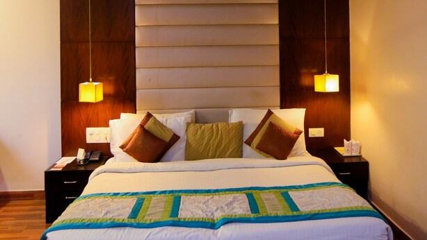Ein modernes Hotelzimmer mit einem großen Bett, einem hölzernen Kopfteil, zwei Nachttischlampen und einem Deckenventilator.