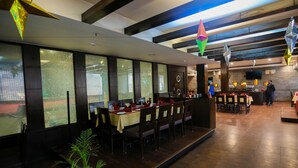 Ein Restaurant mit einer langen Theke, mehreren Tischen und Stühlen. Es gibt dekorative Hängeornamente und einen Blumentopf.