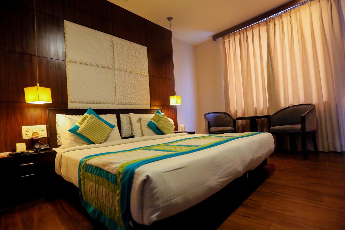 Una habitación de hotel con una cama grande, dos mesitas de noche, una silla y una ventana con cortinas.