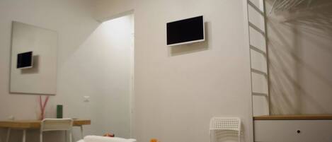 A bedroom with a bed, a desk, a chair, a TV, and a wardrobe.