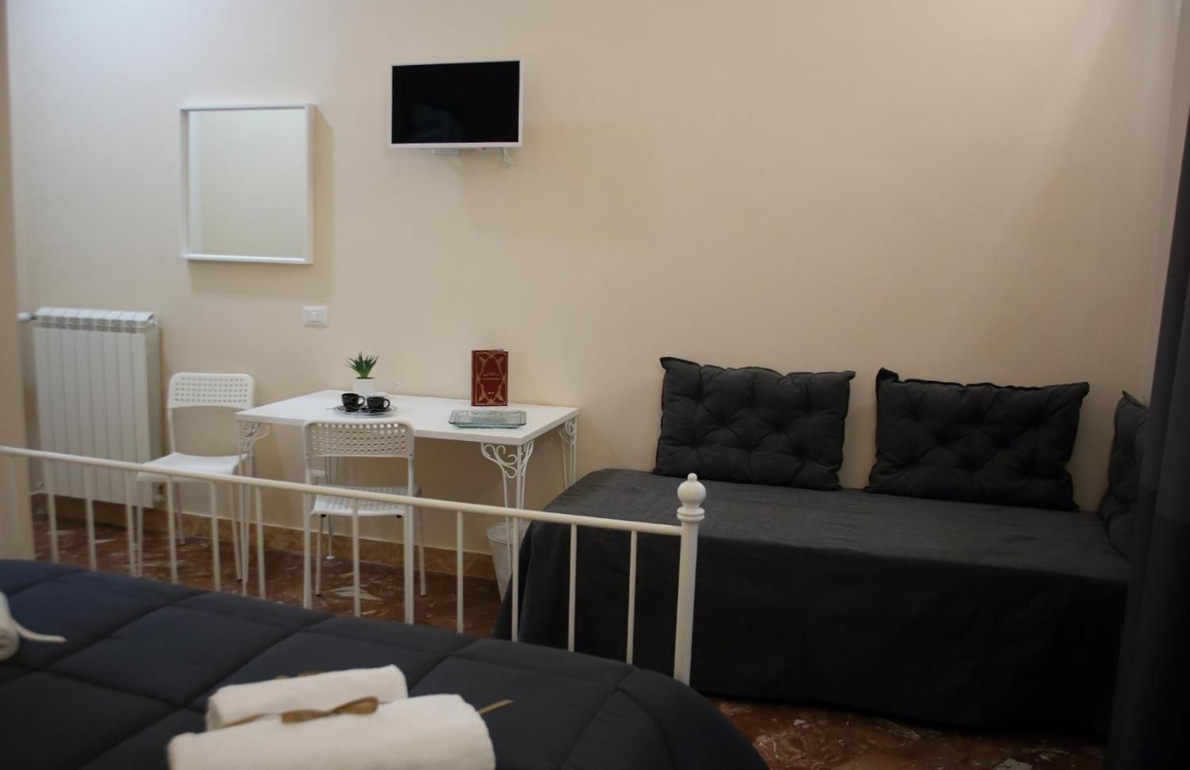 A small, furnished room with a bed, a desk, a chair, and a television.