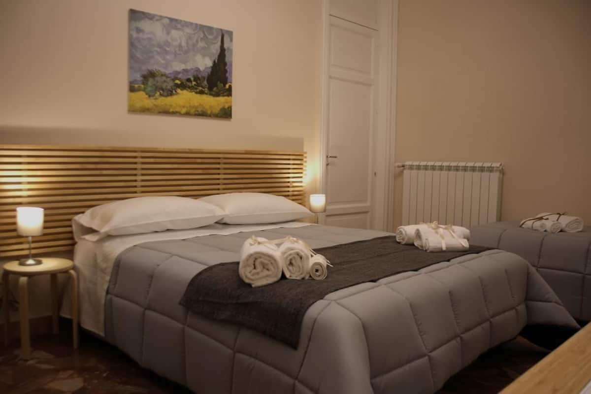 A bedroom with a large bed, a bedside table with a lamp, a radiator, and a painting on the wall.