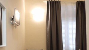 A small, cozy room with a bed, a table with chairs, a TV, and curtains. - Mantegna Rooms (Palermo)