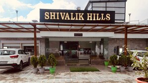 La entrada a Shivalik Hills, con mostrador de recepción, plantas en macetas y automóviles estacionados.
