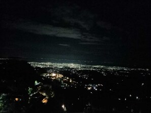 Une vue nocturne d’une ville, avec en arrière-plan une autre ville illuminée par des lumières.