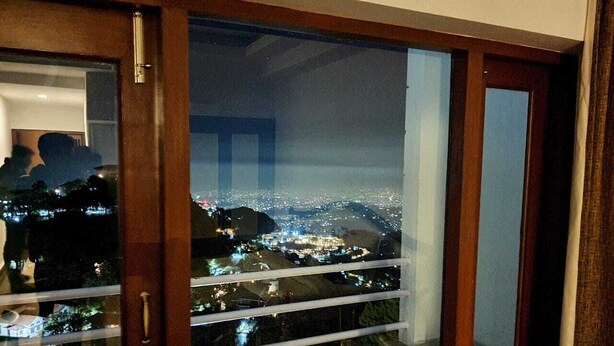 Un balcón con puerta de cristal que ofrece vistas nocturnas de un paisaje urbano con edificios iluminados.