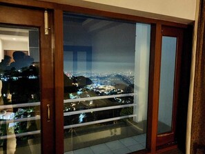 A balcony with a glass door, offering a nighttime view of a cityscape with illuminated buildings. - Shivalik Hills Mussoorie (Dehradun)