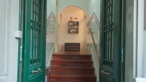 A staircase with wooden steps and green doors, leading to a landing with a shelf of items. - Carolina M Apartment (Porto)