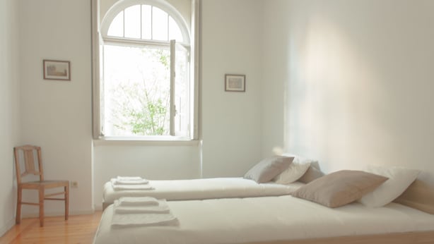 A bedroom with two single beds, a wooden chair, and a large window with an arched top. - Carolina M Apartment (Porto)