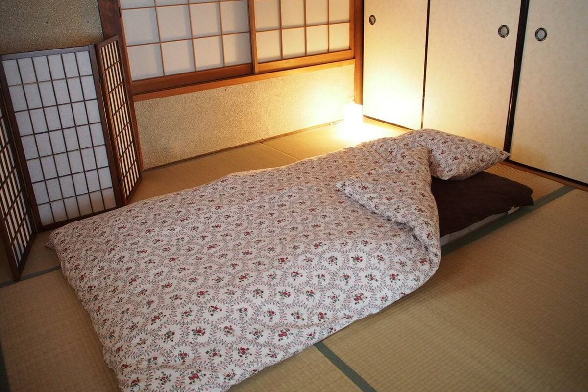 A traditional Japanese room with tatami flooring, a low bed with a floral bedspread, and sliding doors.