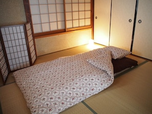 A traditional Japanese room with tatami flooring, a low bed with a floral bedspread, and sliding doors. - GUEST HOUSE TEN-ROKU - Hostel, Caters to Women (Osaka)