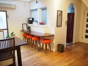 A kitchen with a wooden table, red bar stools, a coffee machine, and a trash can. - GUEST HOUSE TEN-ROKU - Hostel, Caters to Women (Osaka)