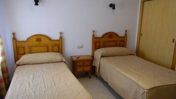 A bedroom with two single beds, a nightstand, a wooden wardrobe, and two wall-mounted light switches.