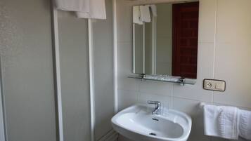 Une salle de bain avec un lavabo blanc, une cabine de douche en verre et un miroir au-dessus du lavabo.
