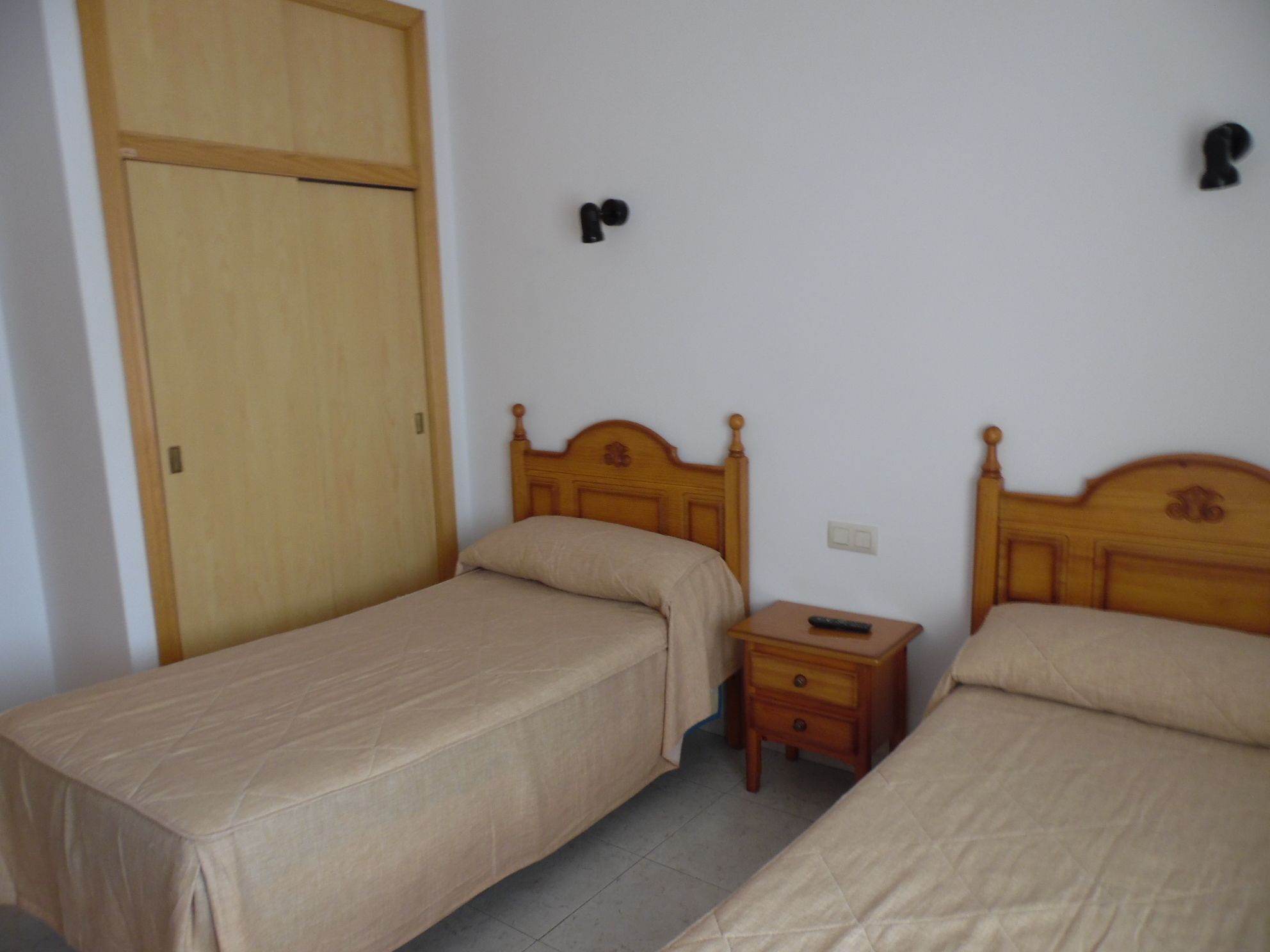 Een kamer met twee eenpersoonsbedden, een houten garderobe, een nachtkastje met een afstandsbediening en een stopcontact.