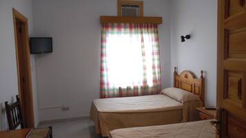 Een slaapkamer met twee bedden, een televisie aan de muur, een raam met geruite gordijnen en een deur.