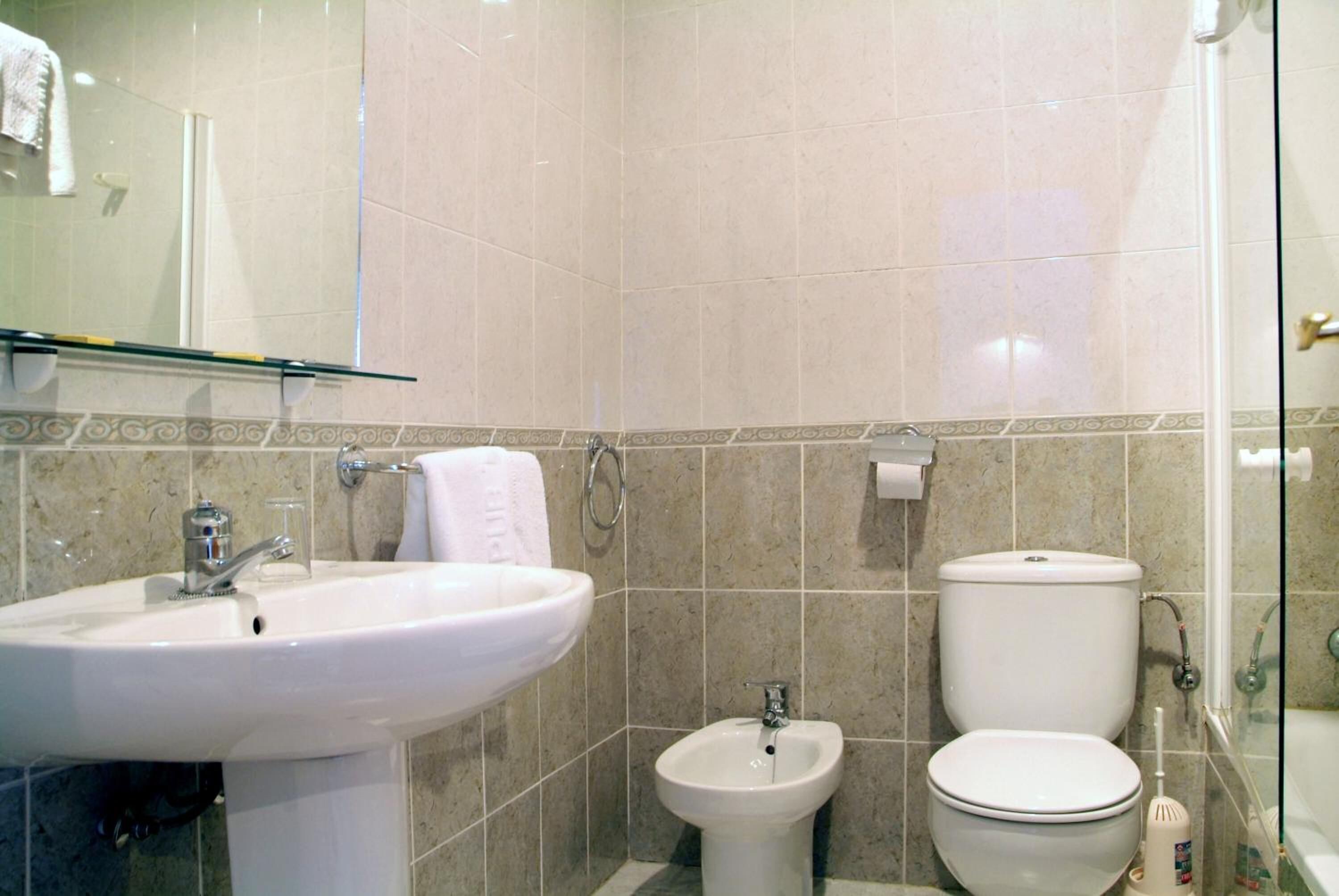 A bathroom with a sink, bidet, toilet, and glass shower enclosure.