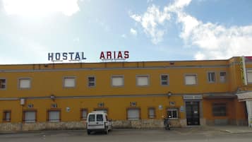 Un edificio con letreros que dicen "HOSTAL" y "ARIAS", una furgoneta estacionada y una motocicleta.