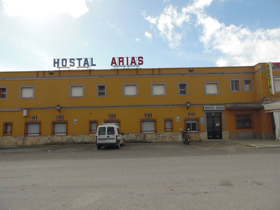 Un edificio con letreros que dicen "HOSTAL" y "ARIAS", una furgoneta estacionada y una motocicleta.