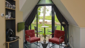 Een kamer met een puntdak, twee rode stoelen, een kleine tafel met een vaas, een televisie aan de muur en uitzicht op koeien en groen buiten.