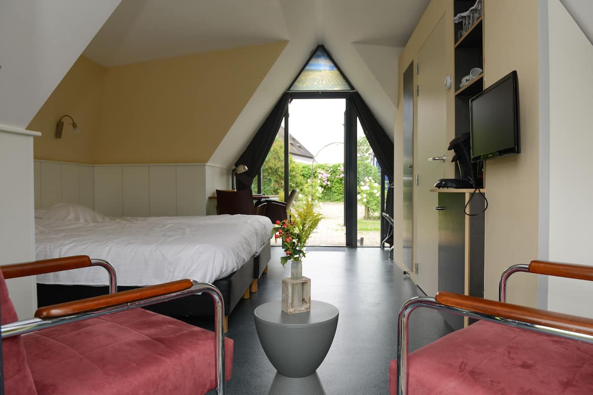 Een slaapkamer met een bed, een bureau en een stoel. Er is een raam met uitzicht op buiten.