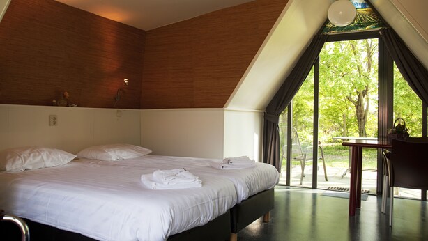 Een moderne slaapkamer met een groot bed, een bureau en uitzicht op groen.