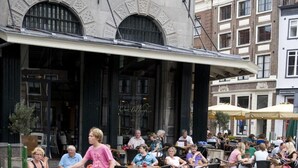 Een terras met stenen vloeren en een gebouw met rondboogvensters op de achtergrond.