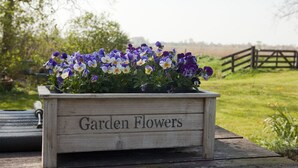Een houten plantenbak met de tekst 'Garden Flowers', gevuld met verschillende paarse en witte bloemen.