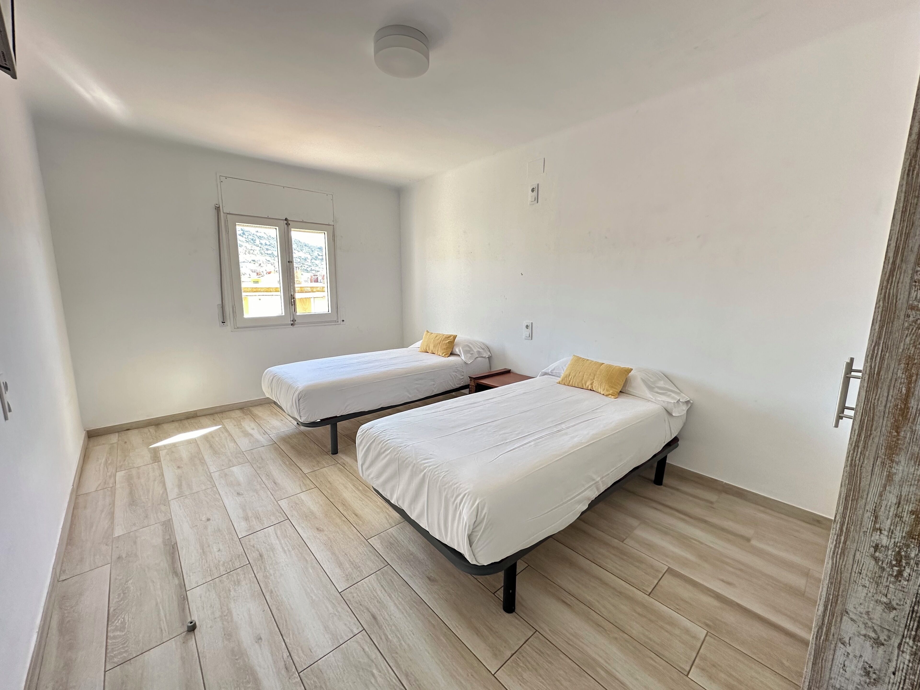 Una habitació amb dos llits, una finestra i una porta.