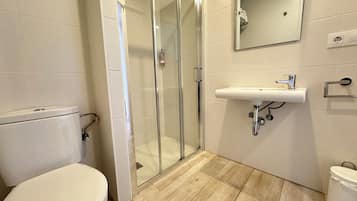 Un baño moderno con inodoro, ducha con mampara de vidrio, lavabo y espejo.
