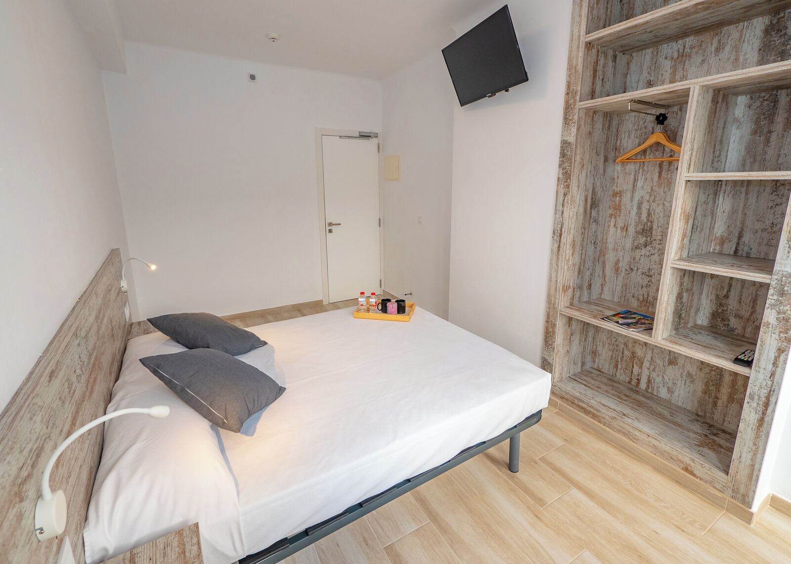 A bedroom with a bed, bedside lamp, and a TV mounted on the wall.
