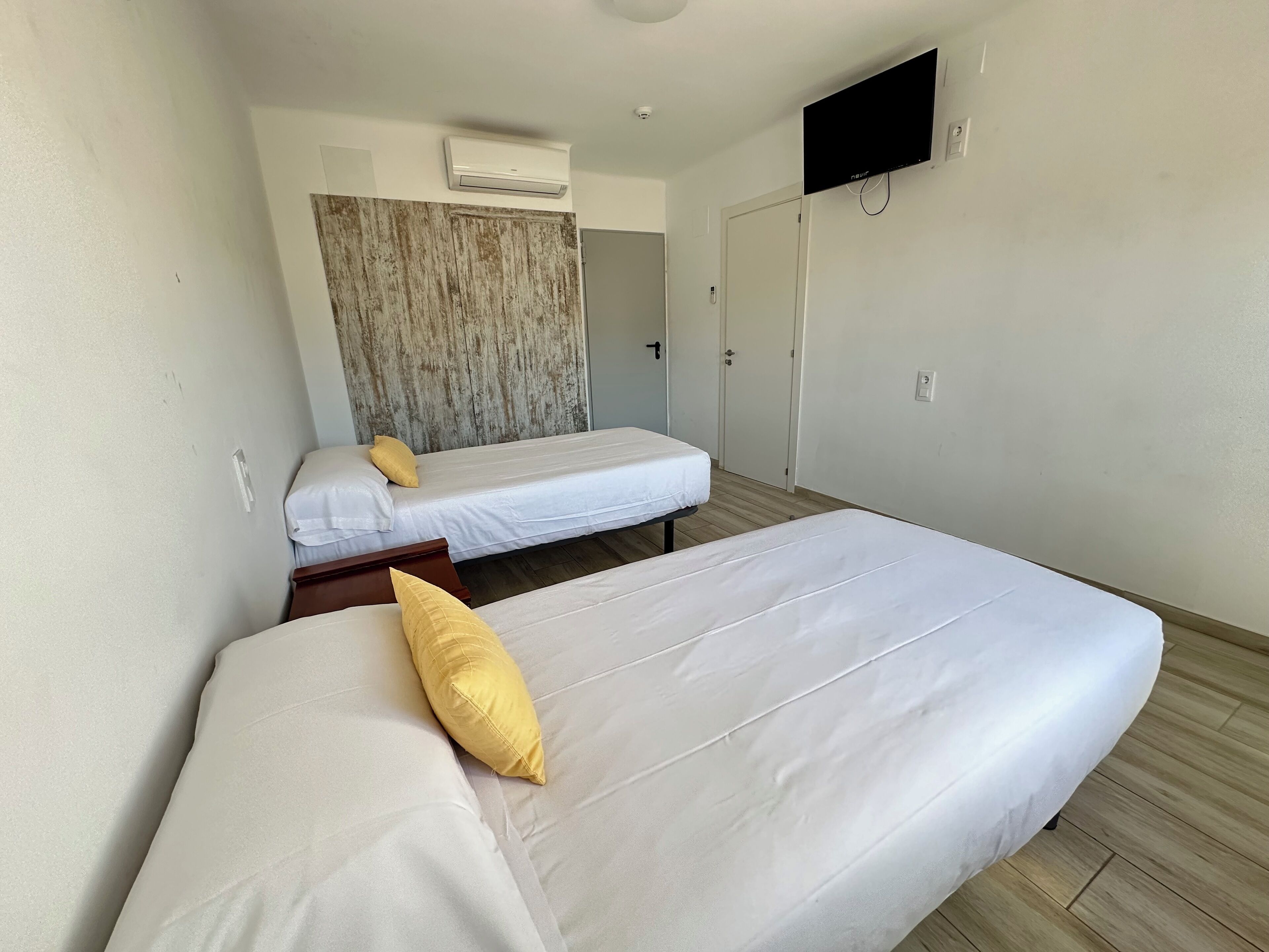A hotel room with two beds, a TV mounted on the wall, and an air conditioning unit.