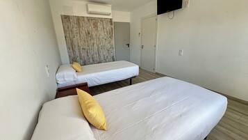 A hotel room with two beds, a TV mounted on the wall, and an air conditioning unit.