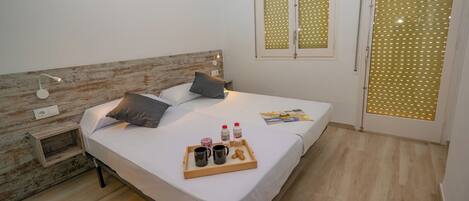 A neatly made bed with pillows, a bedside table with a tray of breakfast items, a wooden headboard, and a window with blinds.