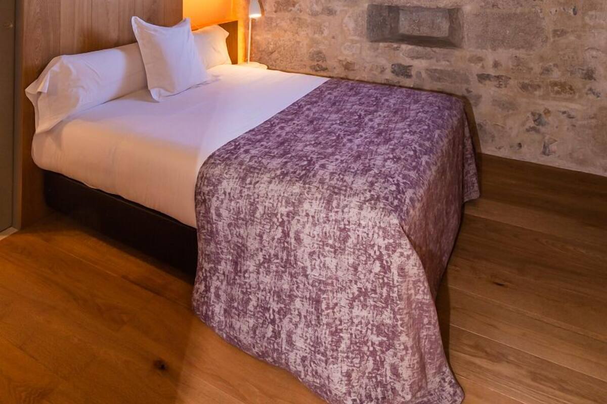A bedroom with a wooden bed, a ceiling fan, a stone wall, and a small window.