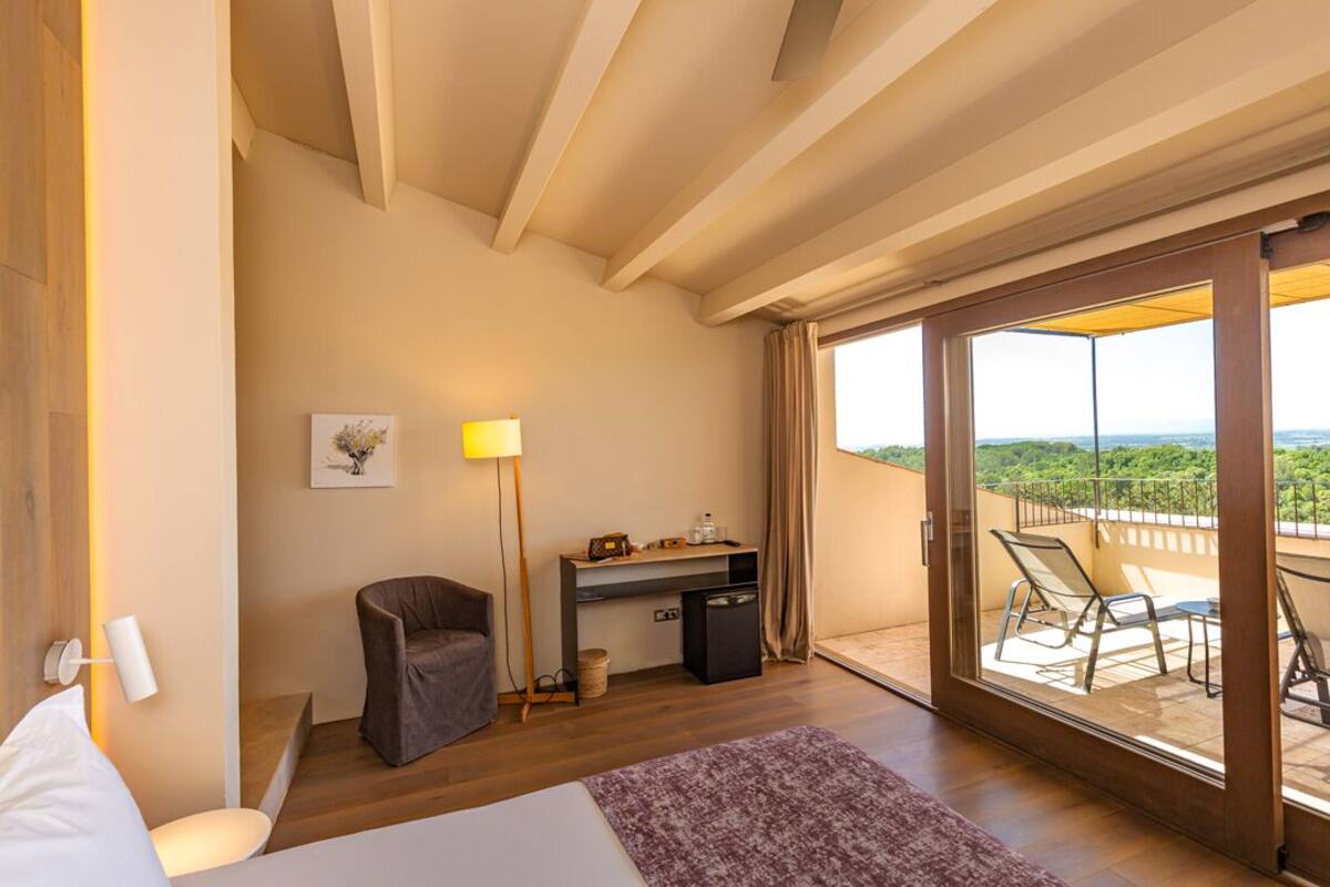 A bedroom with a bed, a desk, a chair, and a balcony with a view.