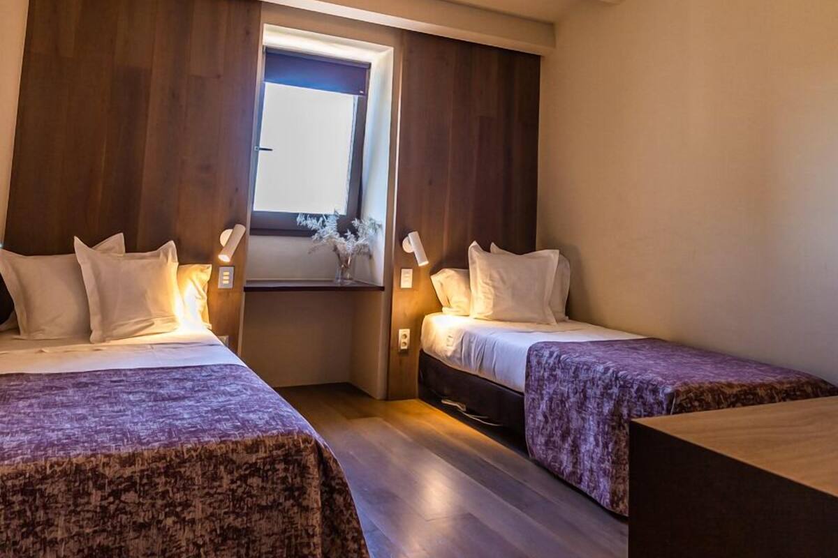 A bedroom with two beds, wooden flooring, a ceiling fan, and a window with a view.