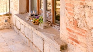 A stone building with arched windows and columns, a tiled floor, and a basket of fruits and vegetables on the windowsill. - Hotel Mas Bosch 1526 (Avinyonet de Puigventos)