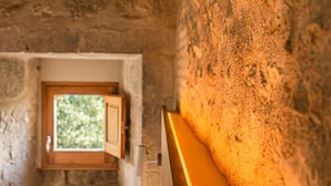 A bedroom with stone walls, a wooden headboard, and a window with a view of greenery. - Hotel Mas Bosch 1526 (Avinyonet de Puigventos)