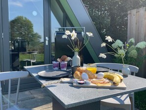 An outdoor dining area with a table set for breakfast, including croissants, eggs, bananas, and a glass of orange juice. - Restinn Medemblik (Wieringerwerf)